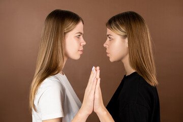 Side view of twin teenage girls touching by hands and looking at one another - obrazy, fototapety, plakaty