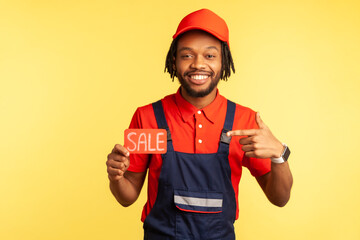 Handsome positive handyman or mechanic wearing red T-shirt and blue uniform, pointing at cad with...