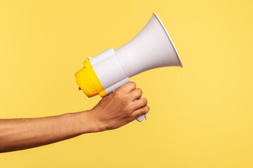 Profile side view closeup of human hand holding megaphone, announcing of advertisement. Indoor studio shot isolated on yellow background.