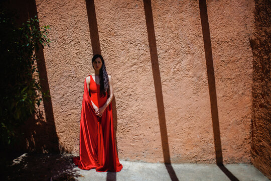 Mature woman wearing red cape and dress standing in front of wall