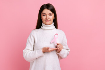 Portrait of calm beautiful woman standing holding rose ribbon in front of chest, female healthy,...