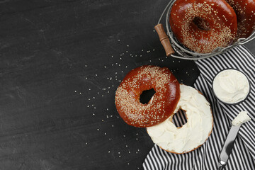 Delicious bagel with cream cheese on black table, flat lay. Space for text
