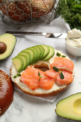 Delicious bagel with cream cheese, salmon and avocado on white marble table