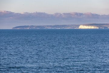 A scenics majestic view of the sea from the sea with white cliff and hill in the background under a beautiful blue sky and some low white clouds