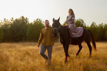 A rural couple with a horse in a natural yellow landscape on an autumn day. Young man and woman together with an animal