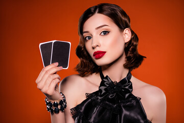 Photo of attractive stunning young woman hold hands cards luck fortune play isolated on dark orange...