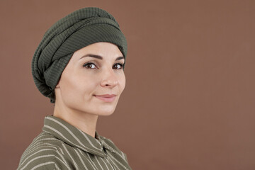 Horizontal close-up studio portrait of beautiful Muslim woman wearing turban on head looking at camera, brown background