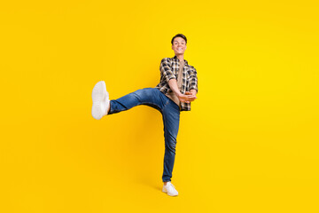 Fototapeta na wymiar Photo of funny crazy guy dance hold hands raise leg wear plaid shirt jeans sneakers isolated yellow color background