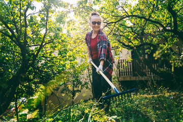 Happy beautiful senior woman 60 years old working in her garden using a rake. Garden care and an...