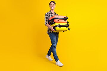 Fototapeta na wymiar Photo of nice guy carry stack suitcase walk wear checkered shirt jeans footwear isolated yellow color background