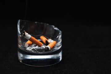 A smoked cigarette in an ashtray on a rough background.