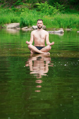 A man meditates in the lotus position, sitting on a stone in the middle of a mountain river. Meditation and peace..