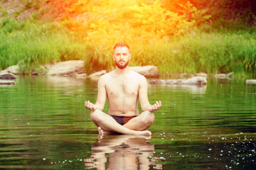 Meditation and peace. A man meditates in the lotus position, sitting on a stone in the middle of a mountain river..