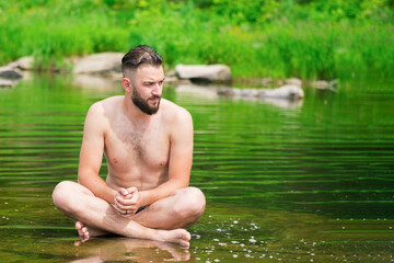 A man meditates in the lotus position, sitting on a stone in the middle of a mountain river. Meditation and peace..