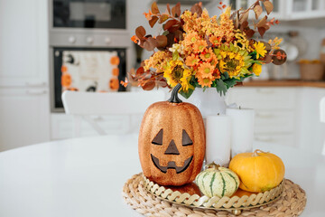A vase of flowers,a jack pumpkin and candles on a tray. In the background - the interior of a white kitchen in Scandi style. The concept of home and comfort. Autumn decor for the Halloween holiday. - Powered by Adobe