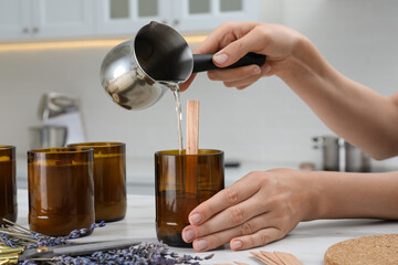Woman making homemade candle at table in kitchen, closeup