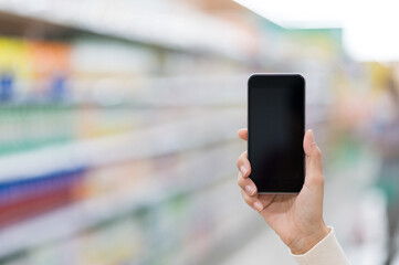 A hand female holding blank screen of smartphone on blurred​ background in supermarket.
