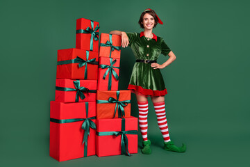 Photo of dreamy adorable young lady elf costume headwear standing gifts pile smiling isolated green...