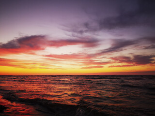 Photo from a sand, wet beach in Latvia of red-orange-yellow sunset reflecting in stormy Baltic Sea