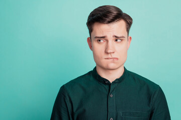 Portrait of doubtful minded smart guy look side empty space bite lip on turquoise background