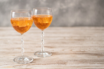 Two glasses of orange cocktails with ice on a wooden table. Aperol spritz recipe made at home.