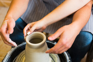 Fototapeta na wymiar Pottery making. Smeared in clay hands of man and woman on potter's wheel. A couple is making a vessel or a bowl or a vase