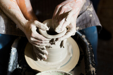 Pottery making. Smeared in clay hands of man and woman on potter's wheel. A couple is making a vessel or a bowl or a vase