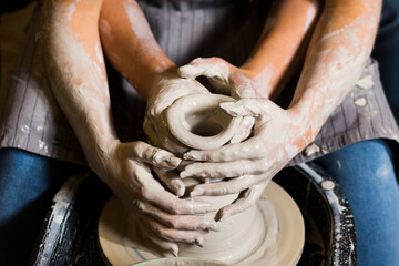 Pottery making. Smeared in clay hands of man and woman on potter's wheel. A couple is making a...