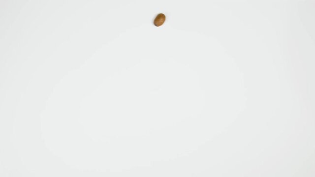 The coffee beans spin rotate quickly fast fly, dispart, splash to the sides with centrifugal coriolis force. The video is in reverse. Coffee beans twist, create pattern, make design shape circle.