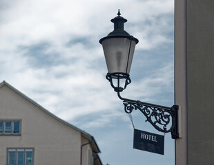 Fototapeta na wymiar Zurich switzerland sept. 13 2021: old lantern with dirty hotel sign in front of blue sky and house facade, light blue colored picture, on day without people