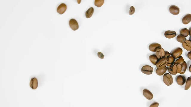 The coffee beans spin rotate quickly fast fly, dispart, splash to the sides with centrifugal coriolis force. The video is in reverse. Coffee beans twist, create pattern, make design shape picture.