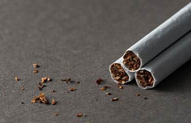 Three cigarettes on a gray background. Scattered tobacco