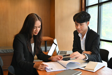 Photo of young business team working together at the wooden meeting table that surrounded by a white screen laptop and document folder.