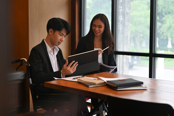 Photo of a handicapped man with a digital tablet works with his assistant in the meeting room.