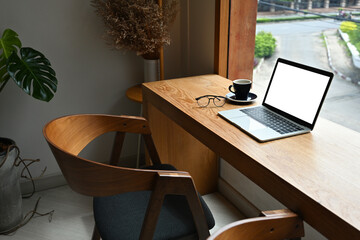 Photo of a wooden counter surrounded by a white blank screen laptop computer and various accessories, Cozy workplace concept.