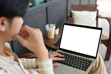 Behind shot of a young smart man using a white screen laptop computer while sitting at a restaurant outdoors.
