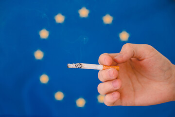 Hand and cigarette on the background of the flag of EU.
