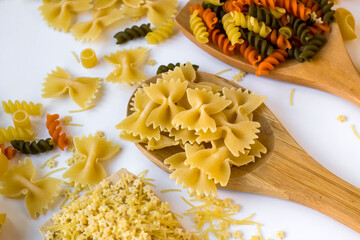 Selected uncooked,dry bow-tie pasta or farfalle pasta on wooden spoon on white surface