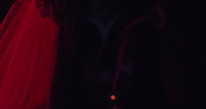 Image of a Calavera girl with a red veil terribly blowing out a candle in a dark Halloween forest
