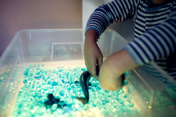 Child plays in the light sensor box with hydrogel, children's hands play with blue water beads and marine life toys, Sensory development and Montessori, themed activities with children