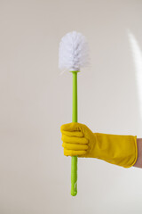 A hand in a yellow rubber glove holds a toilet brush. Toilet bowl cleaning. Professional cleaning of apartments and houses. Dirty job