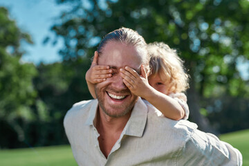 Close up portrait of little son covering dad eyes with hands while they are playing together in the...