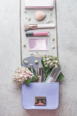 Little lilac handbag with hydrangea flowers and various cosmetics. Beauty concept