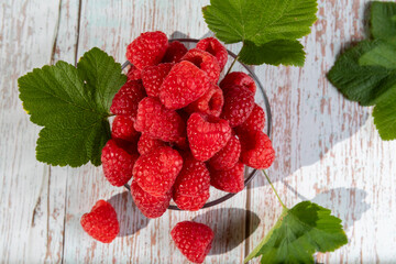 A glass bowl with scarlet ripe raspberries on the light old wooden table.