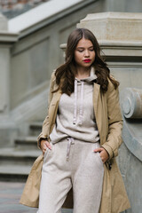 Portrait of fashionable women in beige sports suit and trench coat posing on the street