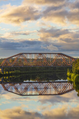 Railway transport bridge made of steel piles and beams across the river during sunset