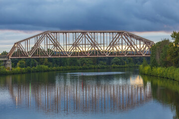 Railway transport bridge made of steel piles and beams across the river during sunset