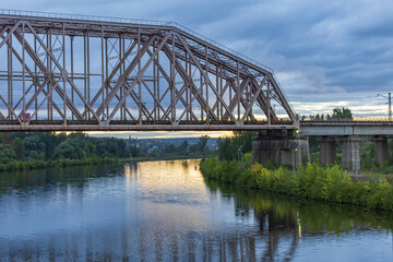 Railway transport bridge made of steel piles and beams across the river during sunset