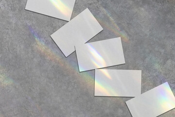 Close up of empty white rectangle business card mockups lying diagonally with rainbow crystal shadows and caustic light effect on light grey concrete background. Flat lay, top view. Open composition. 