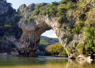 Fototapeta na wymiar Rock Arch Pont D'Arc In The Canyon Of The Gorges De L'Ardeche With Reflections On The River Ardeche In France On A Beautiful Autumn Day With A Clear Blue Sky